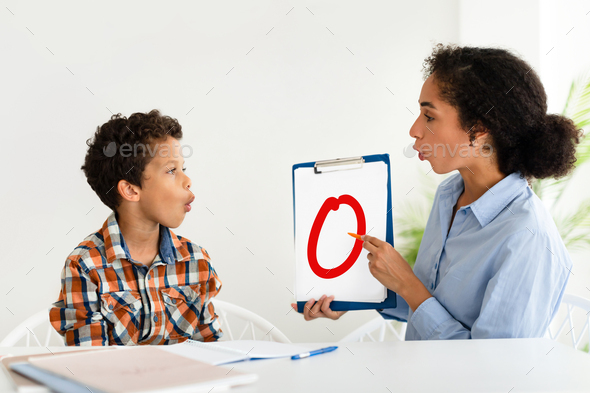 School boy learning letter O with tutor lady sitting indoor