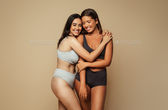 Cheerful millennial latin, arab women in underwear hugs, isolated