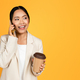 Smiling young asian woman in suit with cup of takeaway coffee talking on smartphone - PhotoDune Item for Sale