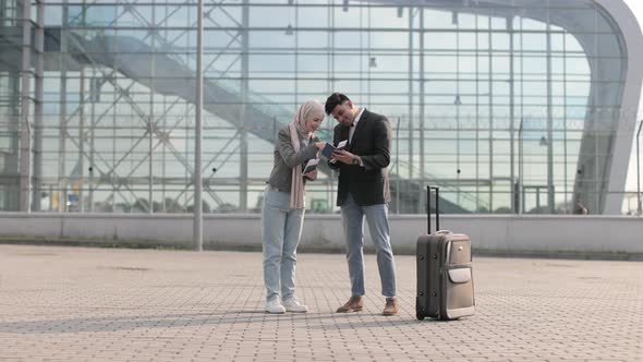 Muslim Lady in Hijab and Arab Man are Glad and Jumping Together Standing Outside Modern Airport alt