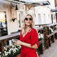 Beautiful woman in sunglasses and a red dress uses a phone near a street cafe - PhotoDune Item for Sale