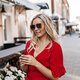 Beautiful woman in sunglasses and a red dress uses a phone near a street cafe - PhotoDune Item for Sale