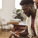 african man using smart phone in office with coworkers in background, young student using cell phone - PhotoDune Item for Sale
