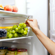 Woman hand taking or picks up bunch of grapes out of open refrigerator or fridge - PhotoDune Item for Sale