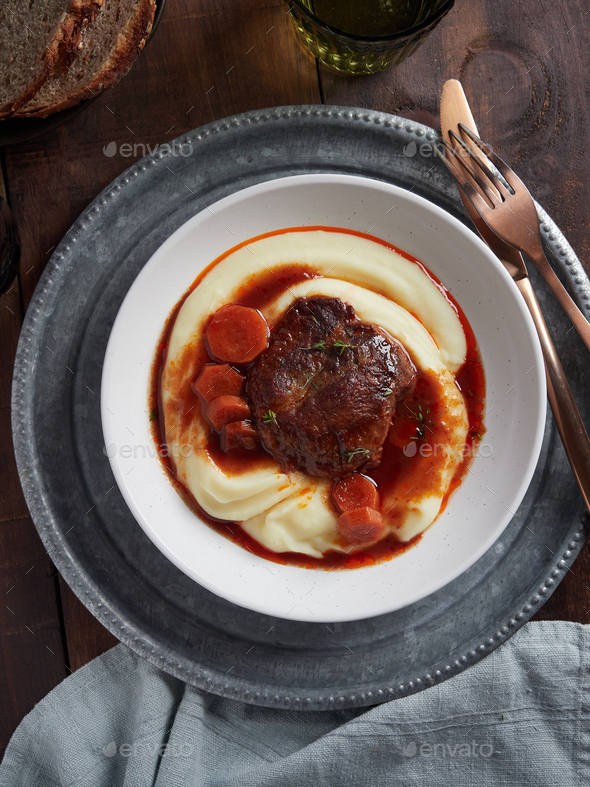 Dish with braised pork cheeks with carrots and gravy over mashed potatoes.
