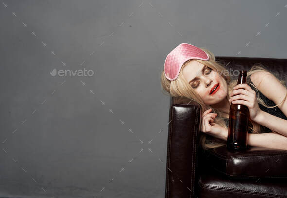 A woman with a pink mask on her head and a bottle of beer sleeps on the couch