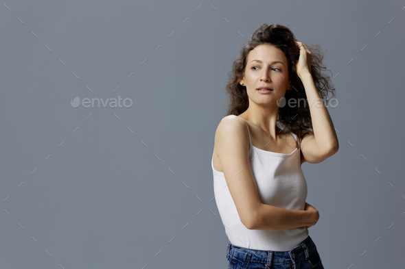 Sexy adorable curly beautiful woman in basic white t-shirt touches hair hugs  herself looks aside Stock Photo by shotprime