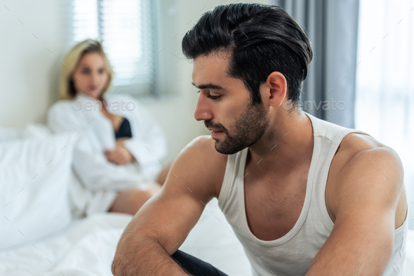 Caucasian young couple sit on bed with painful after fight argument.