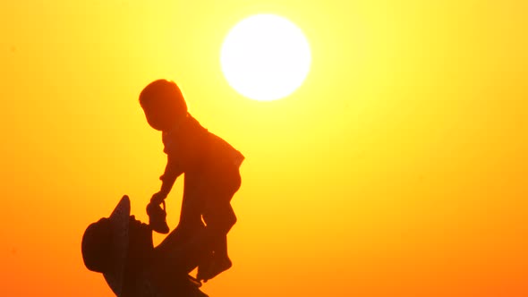 Silhouette of a Happy Mother on Vacation Holding His Daughter in the Air on the Beach During Sunset