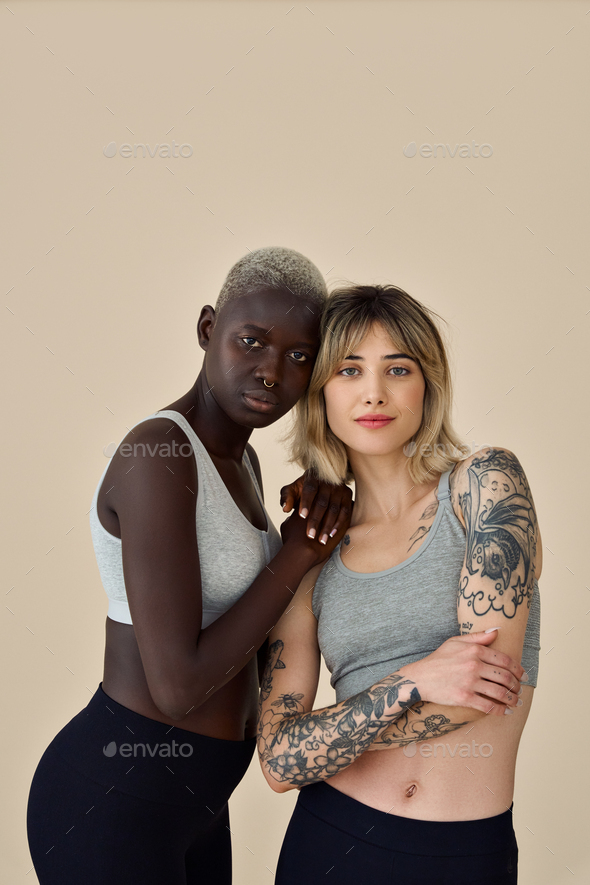 Two cool diverse fit girls wearing sport tops standing on background,  portrait. Stock Photo by insta_photos