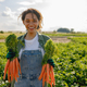 Smiling female farmer holding freshly picked carrots standing in field. Agro industry concept - PhotoDune Item for Sale