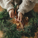 Hands in cozy sweater making Christmas rustic wreath with fir branches, ribbon, pine cones, bells - PhotoDune Item for Sale