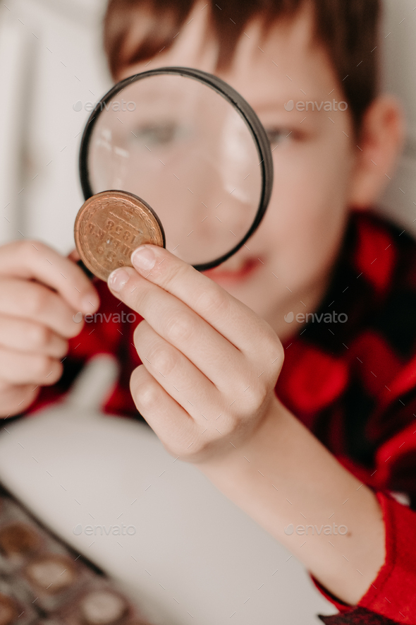 collecting coins. boy examines an old coin through a magnifying