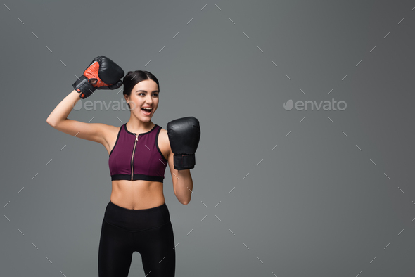 excited sportswoman in boxing gloves showing win gesture isolated on grey