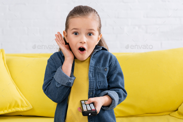 Astonished kid with remote controller sitting on couch