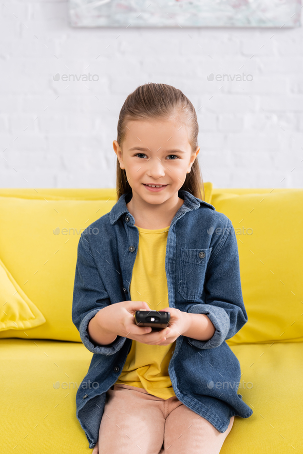 Smiling girl with remote controller sitting on couch