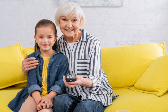 Grandmother with remote controller hugging child on couch