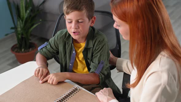 Blind Child Learns to Read Braille Woman Teacher Watches As Boy Kid Moves His Fingers Over the Font alt