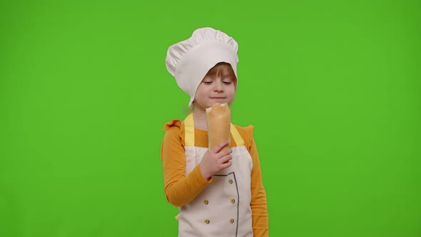 Child Girl Kid Dressed in Apron and Hat Like Chef Cook Eating Fresh Tasty Baguette Fooling Around alt