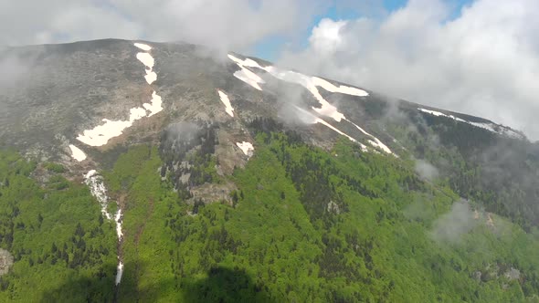 Aerial Forested Mountain With Snow Fragments Among The Clouds in The Spring alt