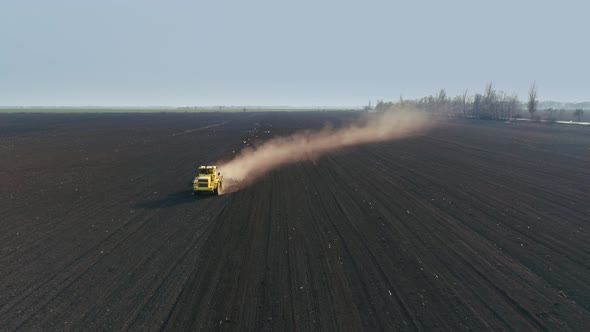 Tractor in the Large Brown Field Prepares the Soil for Sowing alt