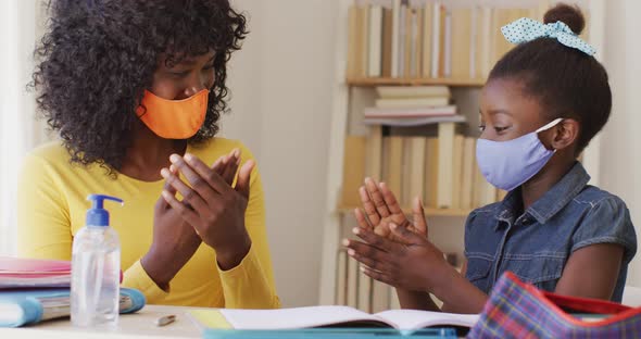 African american mother and daughter wearing face mask sanitizing their hands at home alt