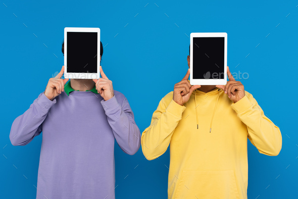 interracial friends with obscure faces holding digital tablets with blank screen isolated on blue