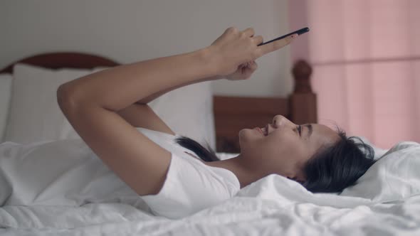 Attractive young Asian woman using a smartphone in the bedroom at home.