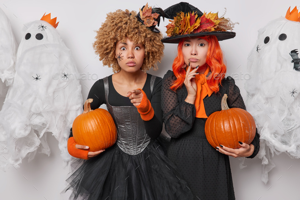 Halloween magic and witchcraft mystery. Two women wear black dresses and wizard hats hold pumpkins
