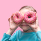 funny girl in a blue t-shirt holds bright pink donuts near her eyes like glasses and looks at you - PhotoDune Item for Sale