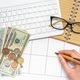 A hand writing a reminder in the organizer at the workplace with cash keyboard glasses notepad - PhotoDune Item for Sale