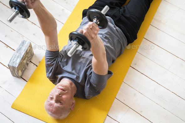 Elderly man exercising with a dumbbells during his workout in home