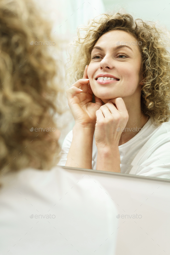 Beautiful woman with curly hair looking into the mirror in a bathroom