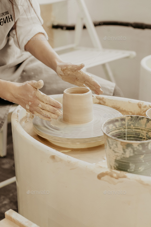 women sculpts a clay pot on a potter\'s wheel from a special wooden tool. Creative workshop.