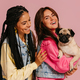 Two beautiful young women carrying cute pug dog and smiling against pink background - PhotoDune Item for Sale