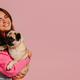 Two joyful young women carrying cute pug dog and making selfie against pink background - PhotoDune Item for Sale