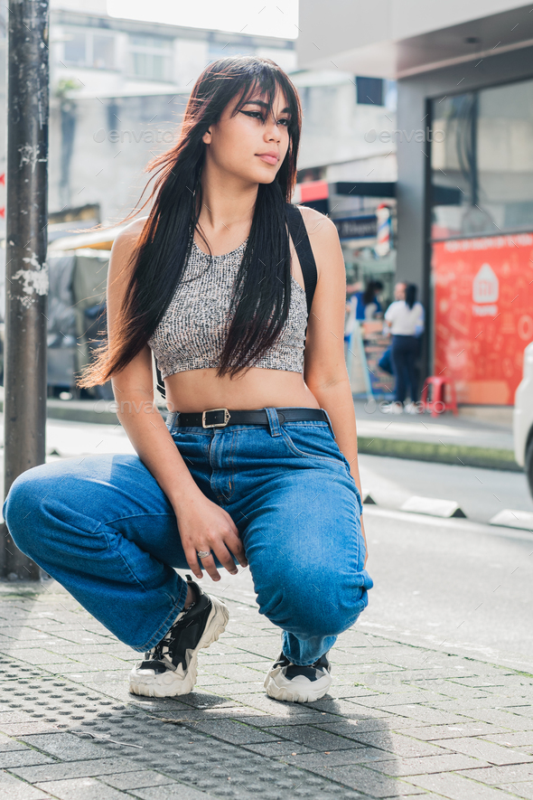 brunette latina girl crouched on the sidewalk posing for photo shoot in the streets