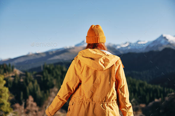 Woman standing in the fall back up her hands up in the mountains nature hike and happiness in yellow