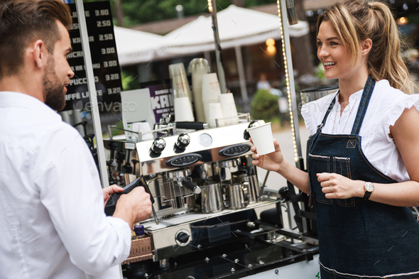Beautiful woman barista selling coffee to the customer