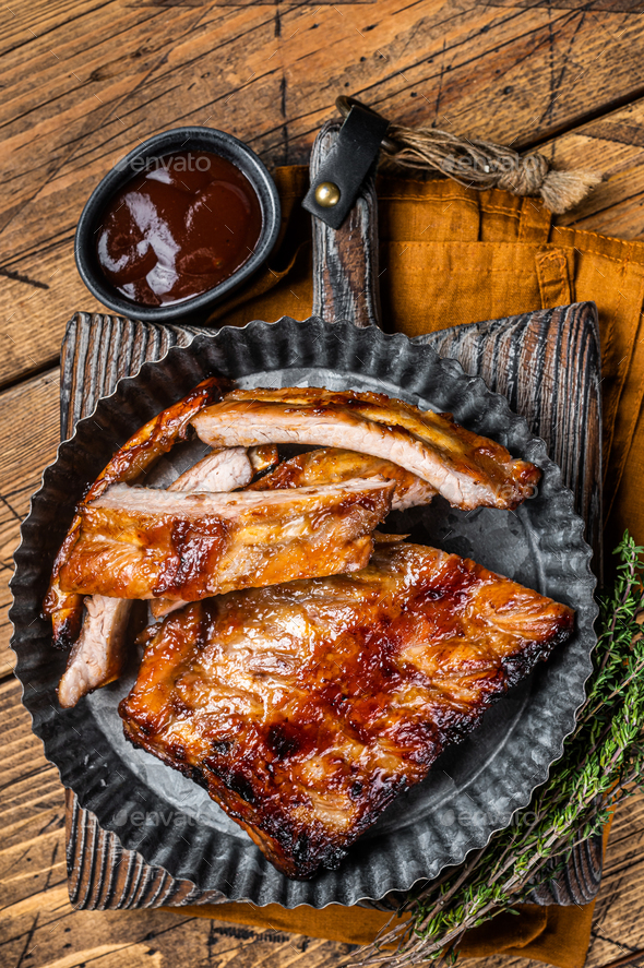 Smoked pork spare ribs glazed in BBQ sauce in a steel plate. Wooden background. Top view