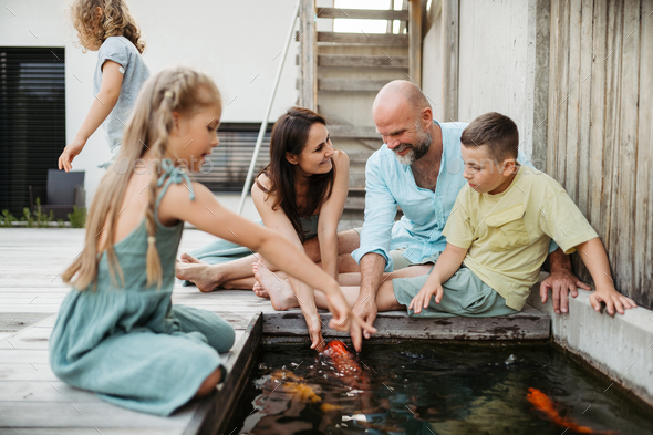 Cheerful family with three kids taking care of fish in pond. Stock