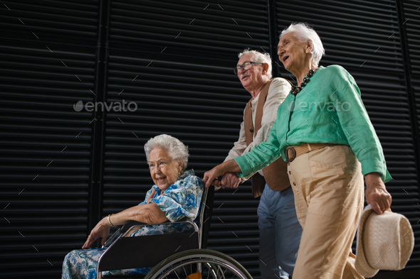 Elderly friends pushing senior woman in wheelchair.