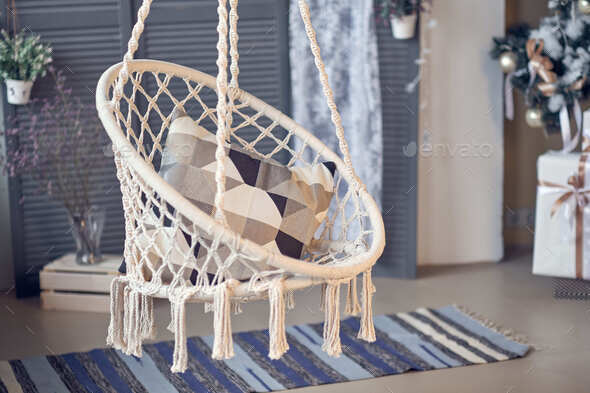 Hanging rope chair in a wooden patio with coffee table and green plant.