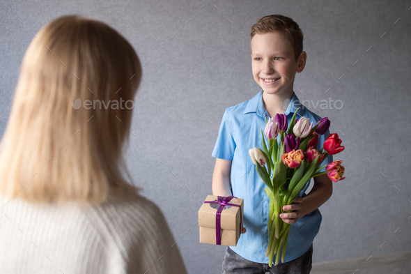 Mom accepts a gift from her son in a blue shirt with tulips in his hands