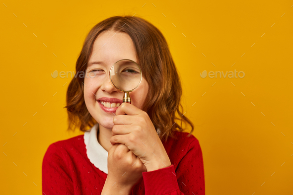 Stylish smiling school teenage girl holding magnifying glass on her eye