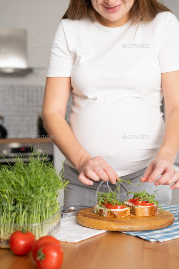 Pregnant young woman preparing healthy sandwiches with microgreens and