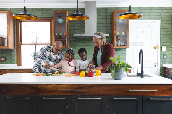 Happy african american grandparents and grandchildren chopping vegetables in kitchen, slow motion