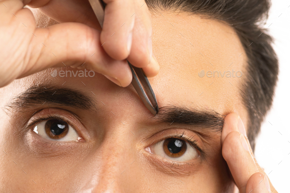 Male eyes and tweezers for eyebrow shape correction