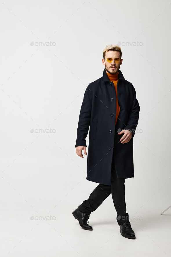 a man in a dark coat and trousers walks to the side on a light background trend of the season model