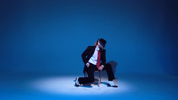 Elegant Man in a Black Hat Is Dancing an Erotic Dance. Spotlight on a Blue Background. alt